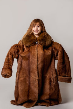 Vertical portrait of a child in a silly mood. Posing in a large natural coat with a fur collar. Imitation and copying of adult parents.