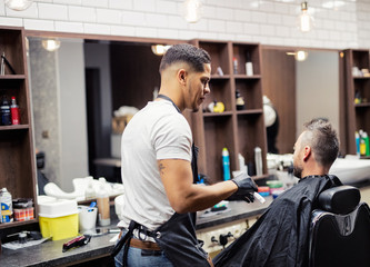 Rear view of man client visiting haidresser and hairstylist in barber shop.