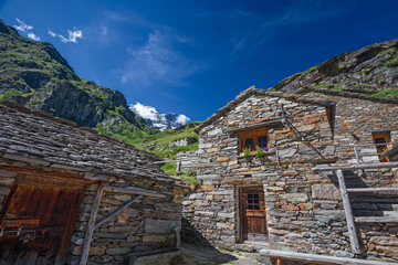 A group of huts on a mountain pasture nestling in a valley on the slopes of Monte Rosa in Piedmont, Italy.