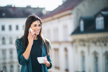 Young businesswoman with smartphone standing on a terrace outside an office in city.