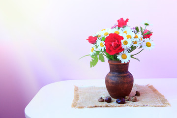 Flowers in pot on lilac background. Chamomiles and red roses in vase on table