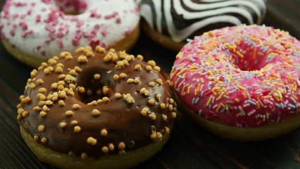 Closeup of composed sweet doughnuts with different glaze and topping served on glassy surface in water drops