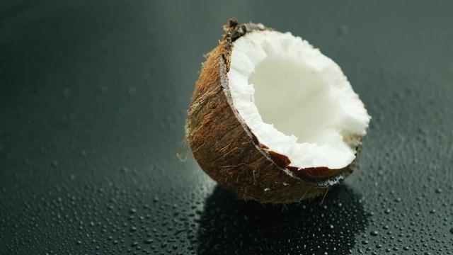 Closeup shot of delicious white coconut half in rough brown shell lying on wet glass surface