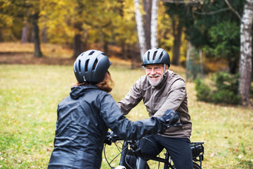 Active senior couple with electrobikes standing outdoors on a road in nature.