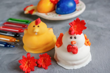 Multi-colored Easter eggs lie next to paint for coloring and marzipan Easter cakes in the shape of chickens