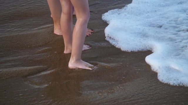 Bare feet of a child and her mom in the waves of the sea.