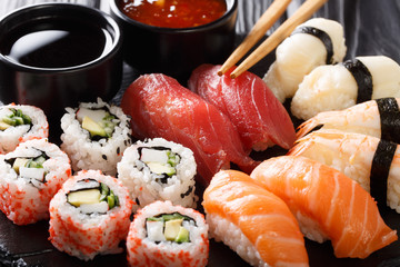 set of Japanese rolls of uramak and sashimi served with two sauces close-up on a slate. horizontal