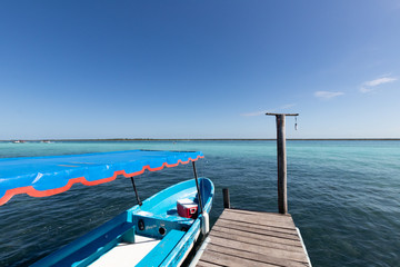 Fototapeta na wymiar wooden jetty for boats on a blue and blue crystalline Caribbean sea with a moored blue boat . Caribbean fishing boat with a dedicated pier