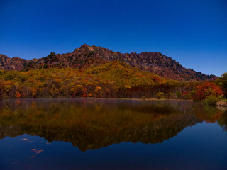 深夜の月明かりで撮影、池ほとりにて遠くの山々を撮影、空には雲が無く星が輝く、山々は紅葉色に染めり、手前の池には鏡の様に写る。
