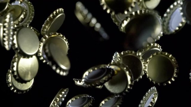 Thrown Beer Lids. Golden beer bottle caps floating in the air on a black background. Slow Motion at a rate of 240 fps