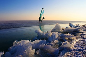 eissurfen auf zugefrorenem see im winter/sport am eis, abendliche stimmung am neusiedlersee in österreich/segel, himmel, schnee, alleine im schnee, blick auf die weite des horizonts
