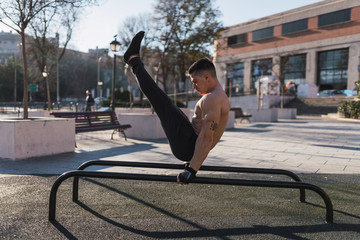 Young guy training on parallel bars with upped legs