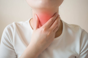 Sick women suffering from sore throat on gray background. Causes of throat pain include flu, common...