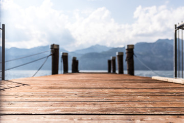 Fototapeta na wymiar Wooden dock pier extending over blue lake water, mountains at lago di garda