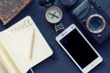 Travel notebook with photo camera, compass and smartphone on black background.