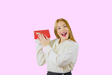 Portrait of a beautiful red-haired girl who is holding a box with gifts lifting him up at the level of his face is smiling enthusiastically at the camera on an isolated background, the concept of