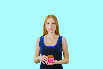 Cute beautiful girl with long red hair holding a box with a gift and looking into the camera on an...