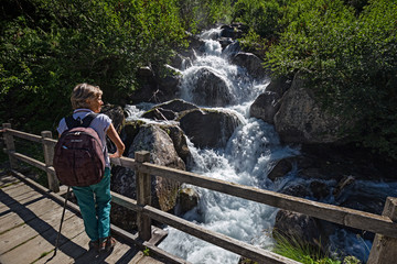 Obraz premium A hiker, she stops on a bridge to observe the rushing waters of a stream.