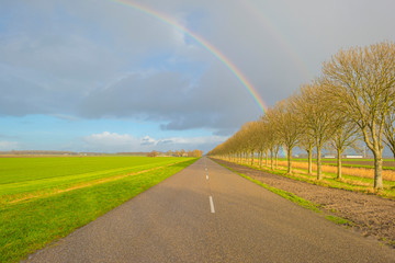 Rainbow over a road in a rulral landscape in sunlight in winter