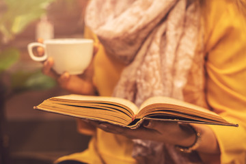 Woman holding book and cup of hot tea drink at cafe