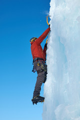 Alpinist man with ice tools axe climbing a large wall of ice. Outdoor Sports Portrait.