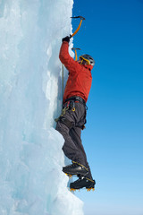 Fototapeta na wymiar Alpinist man with ice tools axe climbing a large wall of ice. Outdoor Sports Portrait.