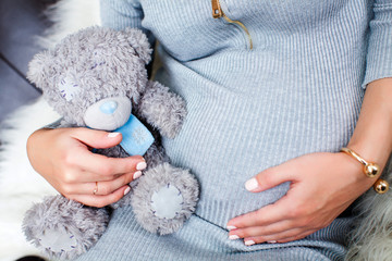 a young pregnant wooman keeps  a Teddy bear toy at hers tum