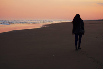 夕暮れの砂浜を歩く女性の後ろ姿