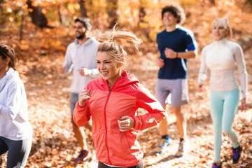 Zelfklevend Fotobehang Joggen Small group of people running in woods in the autumn. Selective focus on blonde woman.
