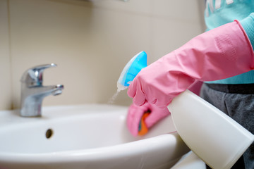 Image of female hands in rubber gloves washing sink in bath