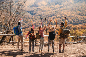 Happy hikers standing on the glade with hands in the air and enjoying the view. Backs turned....