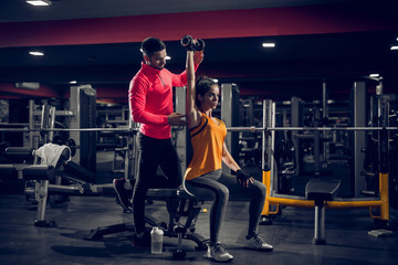 Picture of personal trainer helping her client to lift weight in a gym.