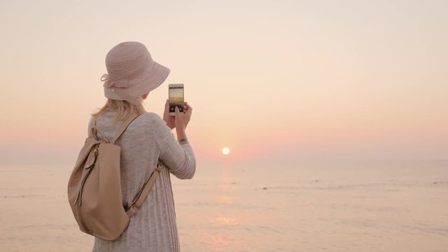 A new day, new opportunities and fulfillment of desires, the girl in the hat fixes the moment of sunrise on the phone