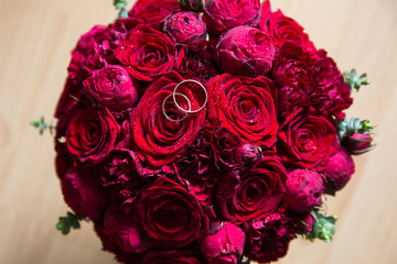 A pair of wedding rings on a bouquet of red roses and peonies, close up shot