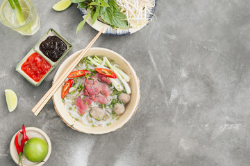 Traditional Vietnamese soup Pho bo with herbs, meat, rice noodles, broth. Pho bo in bowl with chopsticks, spoon. Space for text. Top view. Asian soup Pho bo on wooden table background. Vietnamese soup