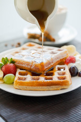 Syrup pouring on breakfast waffles with grapes strawberry and banana