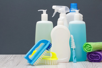Bottles of dishwashing liquid, brushes and sponges on gray background.
