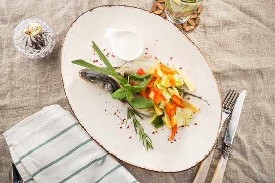 Grilled dorado fish stuffed with different vegetables on white plate served on the table