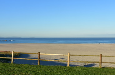 Fototapeta premium Beach with grass and wooden fence. Morning light, sunny day, blue sky. Galicia, Coruna, Spain.