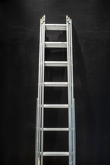 metal staircase stands near a beautifully textured black concrete wall lit from above