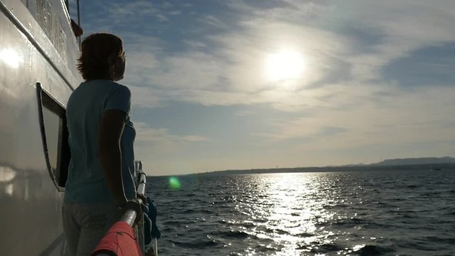 Charmed woman standing on ship`s starboard and looking at sunset in slo-mo  