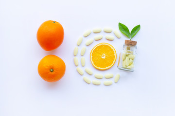 Vitamin C bottle and pills with orange fruit on white.