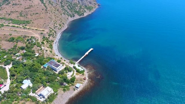Aerial: pier for yachts and sailboats, glare on water, beach of Karadak vulcan, Crimea.