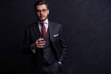 Handsome young business man enjoying a cigarette while standing on black background.