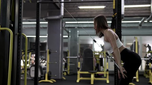 Side View - Beautiful Slim Young Female Fitness Model Doing Simulator Exercise For Back and Arms Muscles. The Concept Of A Strong Enduring Body
