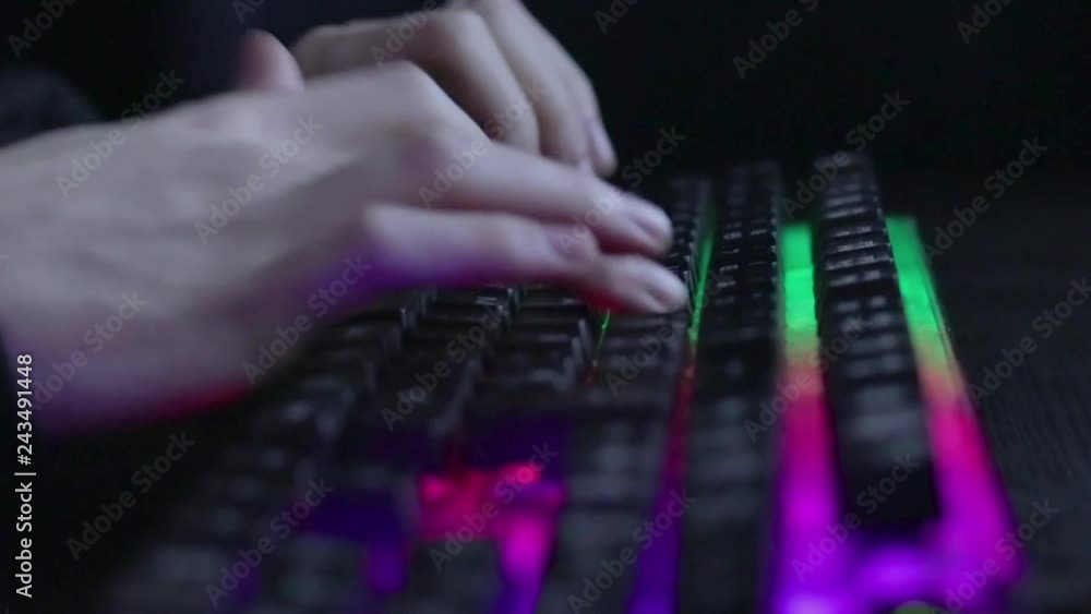 Poster low angle shallow focus view across hands typing on gaming multimedia keyboard with neon lighting.