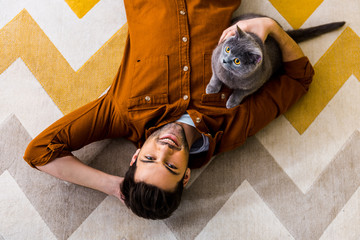 top view of smiling man lying on carpet with british shorthair cat © LIGHTFIELD STUDIOS
