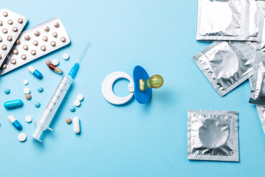 Birth control pills, an injection syringe and condom in a package on blue background. The concept of choosing method of contraception, birth control pills or condom. nipple as symbol of pregnancy.
