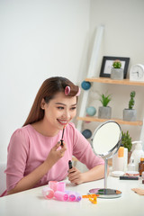 Obraz na płótnie Canvas Serious attractive applying lip gloss and holding mirror in bright living room