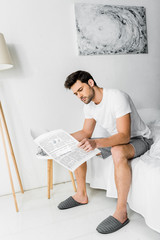 handsome young man in pajamas reading newspaper in bedroom